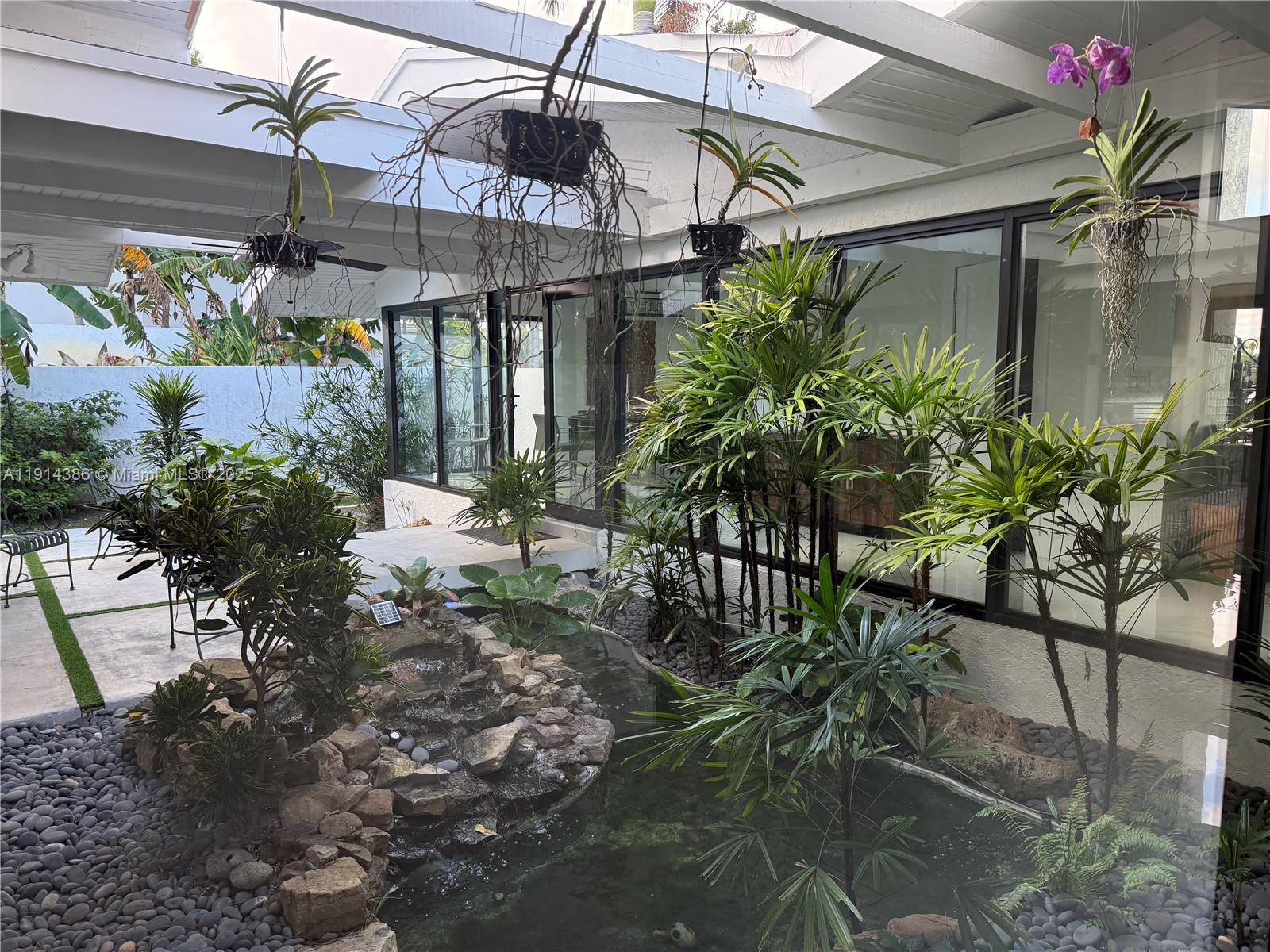 A covered outdoor patio features a stone water feature, lush tropical plants, and hanging orchids — 7521 SW 56th St, Miami FL 33155, MIAMI, FL