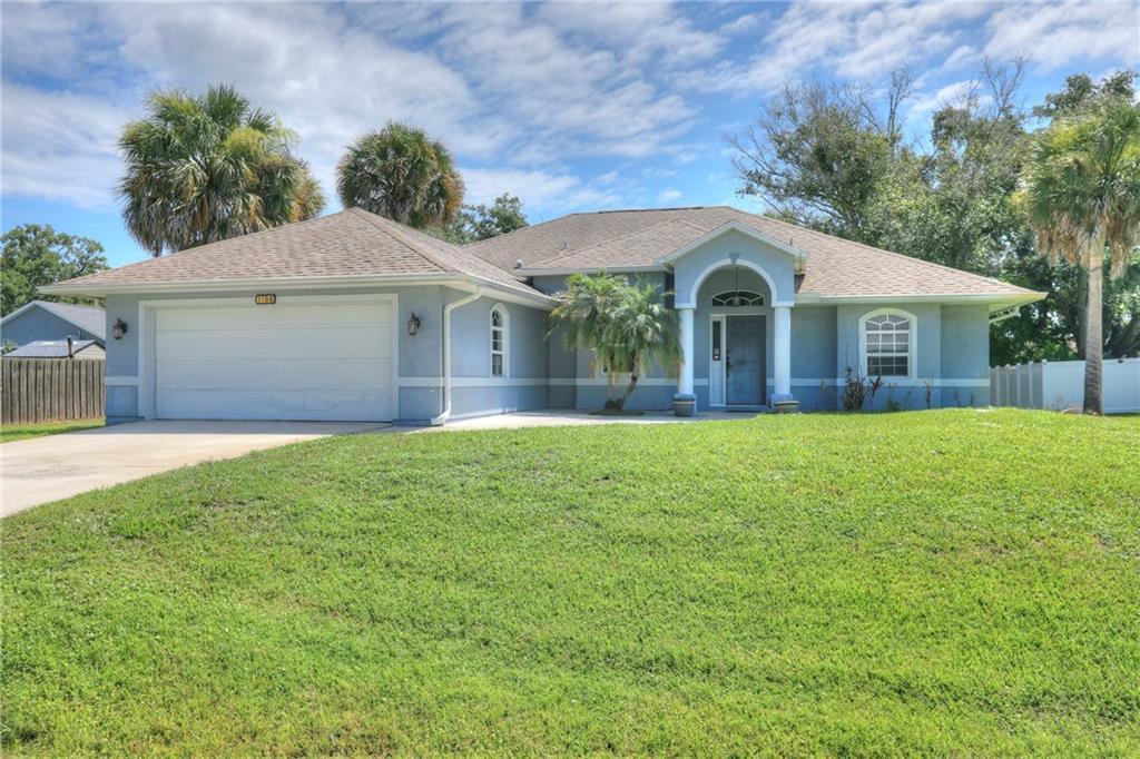 A single-story blue house with a two-car garage and a front lawn under a sky — SEBASTIAN, FL
