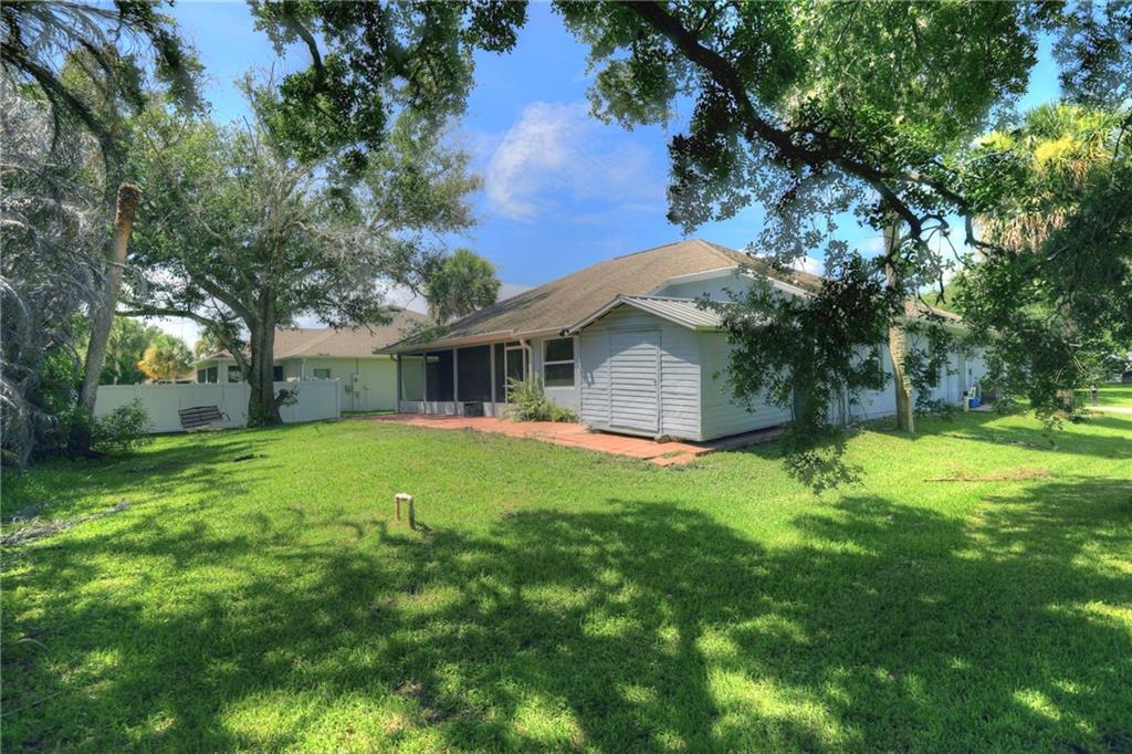 The backyard of a house features a screened-in patio, a storage shed, and large trees — SEBASTIAN, FL