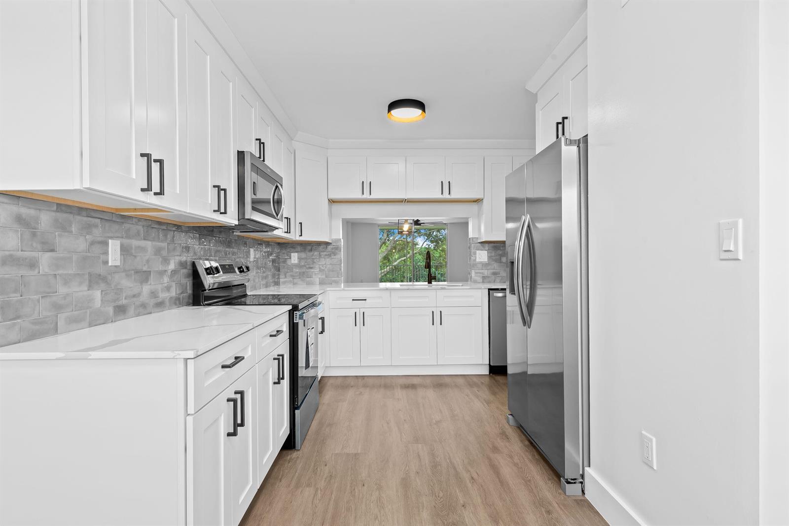 A galley kitchen features white cabinets, stainless steel appliances, and a gray subway tile backsplash — 4734 E Lucerne Lakes Blvd E # 303, Lake Worth FL 33467, LAKE WORTH, FL