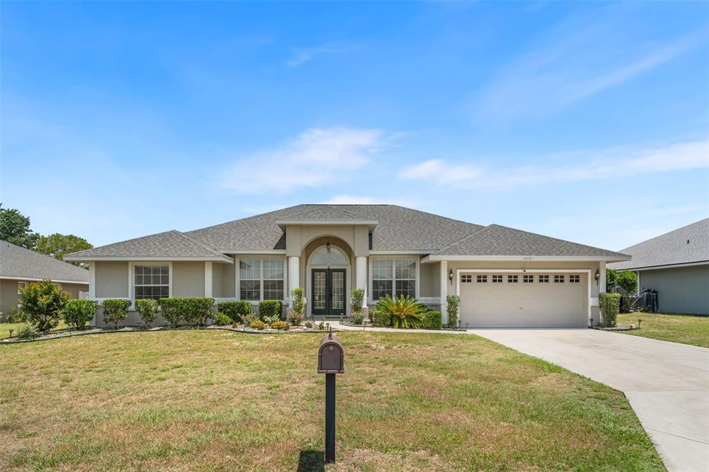 A single-story house with a beige exterior, a gray shingled roof, and a two-car garage — 10161 SE 67TH TERRACE, BELLEVIEW, FL