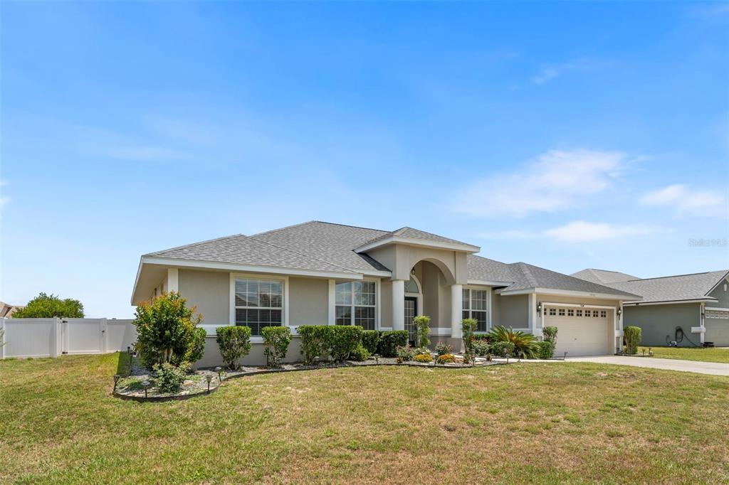 A single-story suburban house with a beige stucco exterior, a garage, and a landscaped yard — 10161 SE 67TH TERRACE, BELLEVIEW, FL