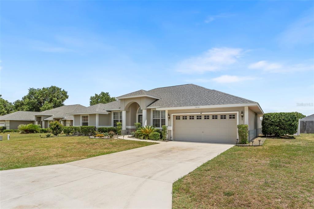 A single-story suburban house features a two-car garage, a concrete driveway, and a landscaped yard — 10161 SE 67TH TERRACE, BELLEVIEW, FL