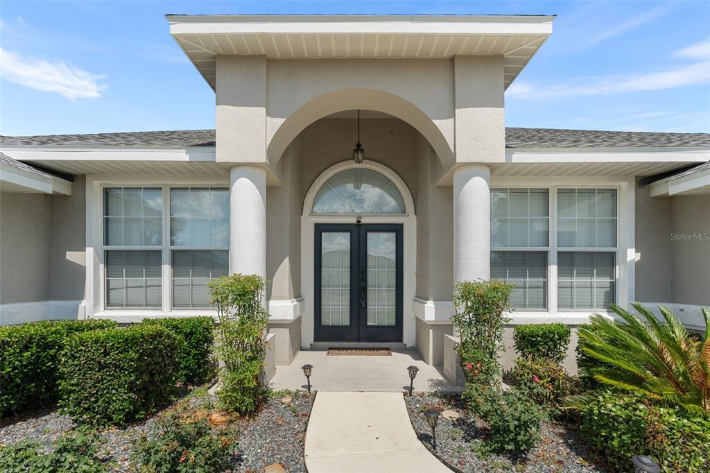 The exterior of a house features a covered entryway with white columns and double doors — 10161 SE 67TH TERRACE, BELLEVIEW, FL