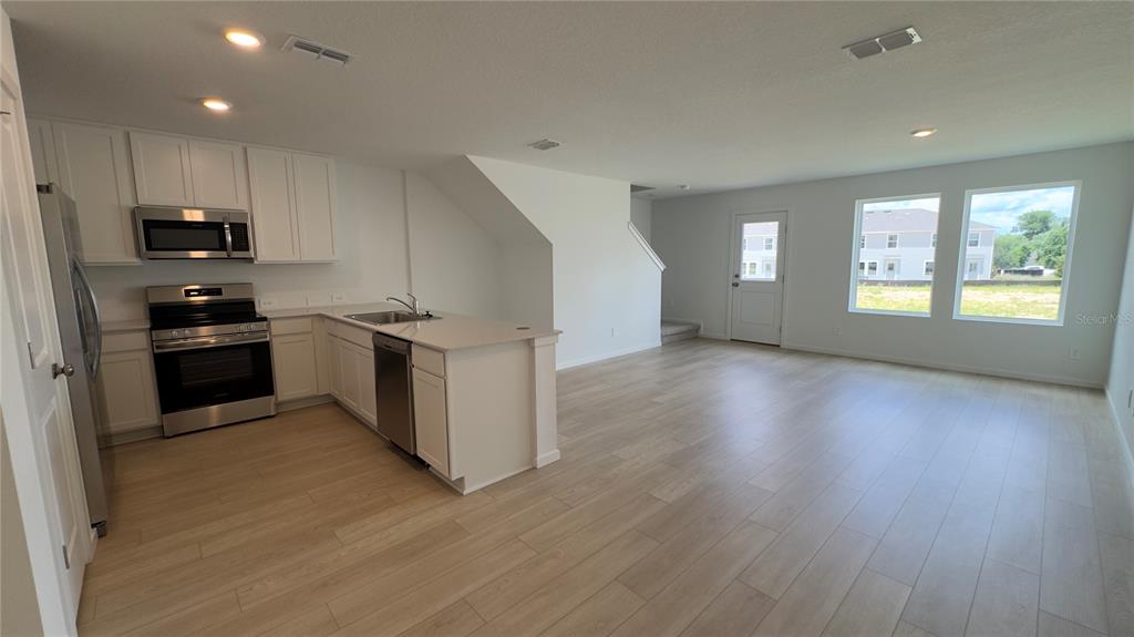 A kitchen with white cabinets and stainless steel appliances opens into a spacious living area — 831 LYNX, DAVENPORT, FL