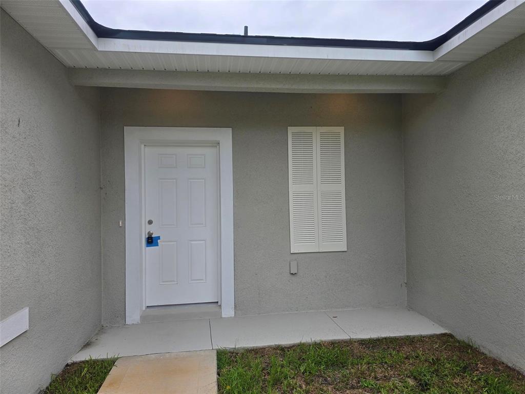 A white front door with a lockbox sits on a concrete porch under an overhang — 208 LOCUST PASS, OCALA, FL
