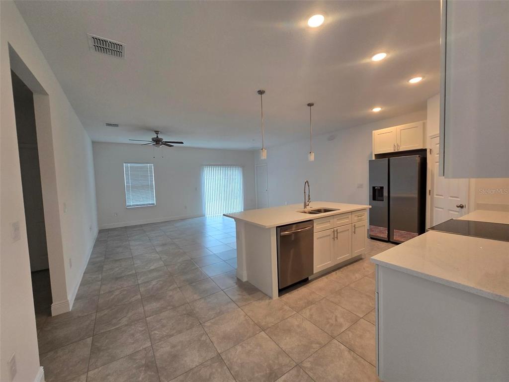 A kitchen with a white island and stainless steel appliances opens into a living area — 208 LOCUST PASS, OCALA, FL