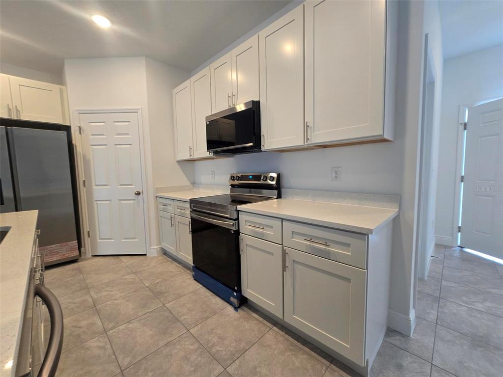 A kitchen features white cabinets, stainless steel appliances, and light-colored countertops — 208 LOCUST PASS, OCALA, FL