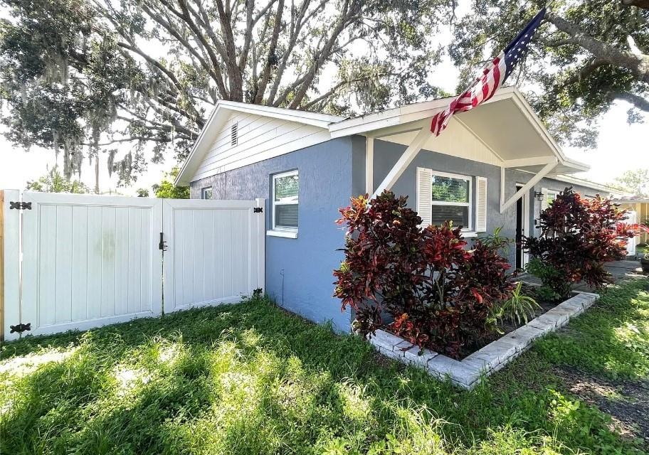 A blue house with a white fence, a front porch, and a large American flag — 8104 BADGER LANE, NEW PORT RICHEY, FL