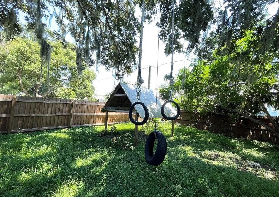 A backyard features a wooden play structure with hanging tire swings and gymnastic rings — 8104 BADGER LANE, NEW PORT RICHEY, FL