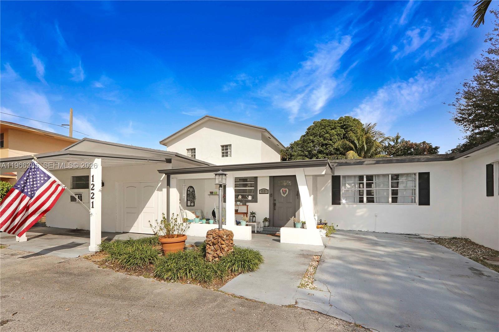 A white single-story house features a covered porch, a carport, and an American flag — 1221 SW 74th Ct, Miami FL 33144, MIAMI, FL