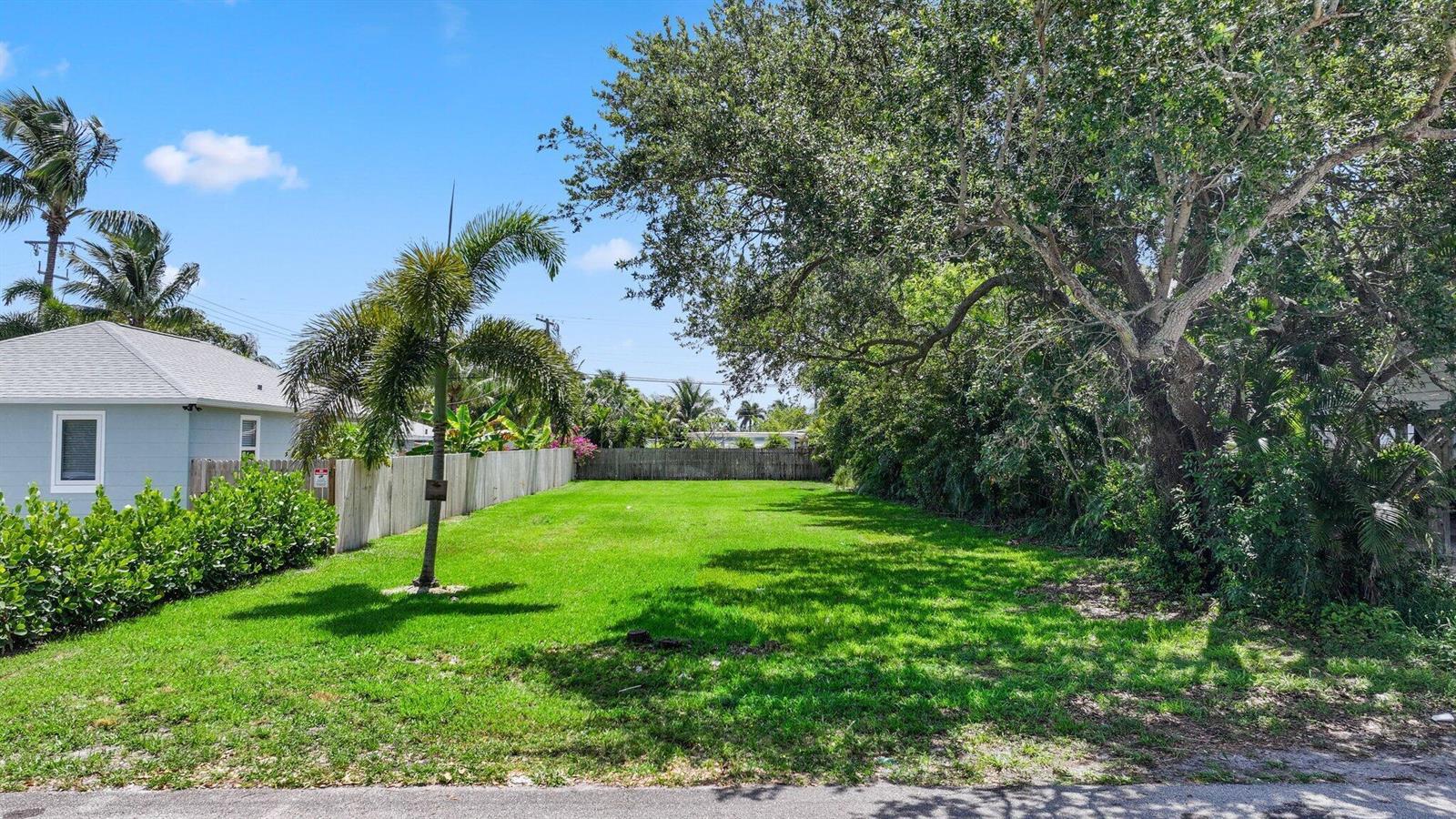 A grassy vacant lot is bordered by a wooden fence and mature trees — 614 N 5th Street, Lantana FL 33462, LANTANA, FL