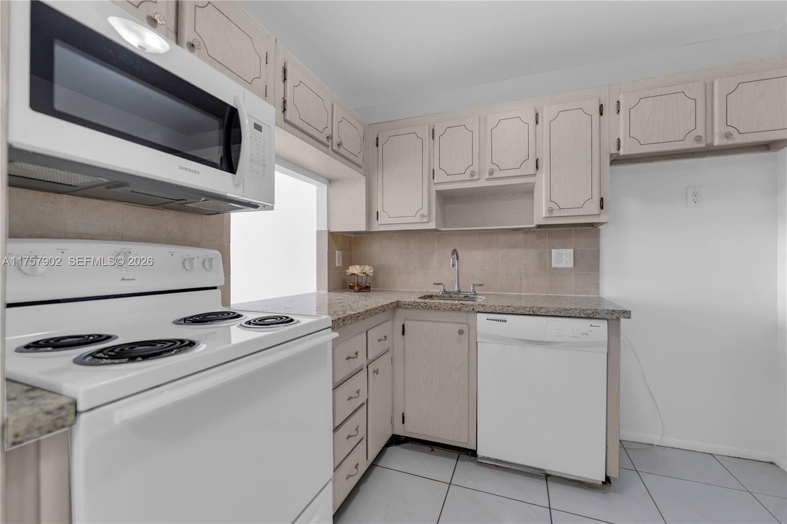 A kitchen features white appliances, light wood cabinets, granite countertops, and tiled flooring — 1817 S Ocean Dr # 827, Hallandale Beach FL 33009, HALLANDALE BEACH, FL