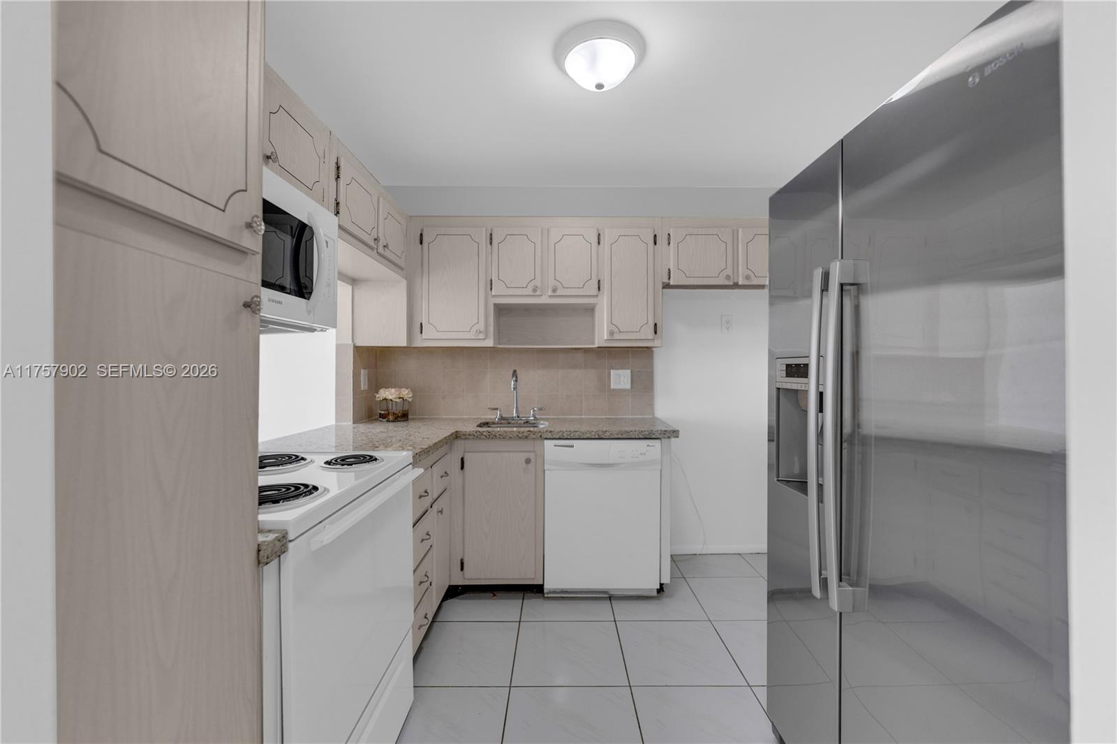 A kitchen features light wood cabinets, white appliances, a stainless steel refrigerator, and tiled floors — 1817 S Ocean Dr # 827, Hallandale Beach FL 33009, HALLANDALE BEACH, FL