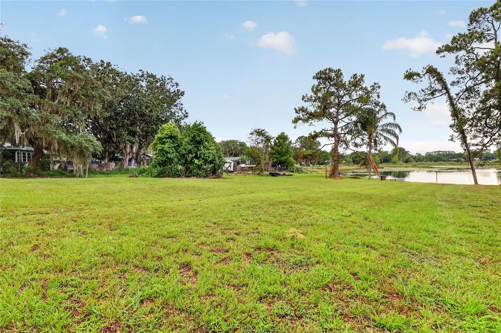 A large, grassy backyard features mature trees and a view of a nearby lake — 37414 TURNER DRIVE, UMATILLA, FL