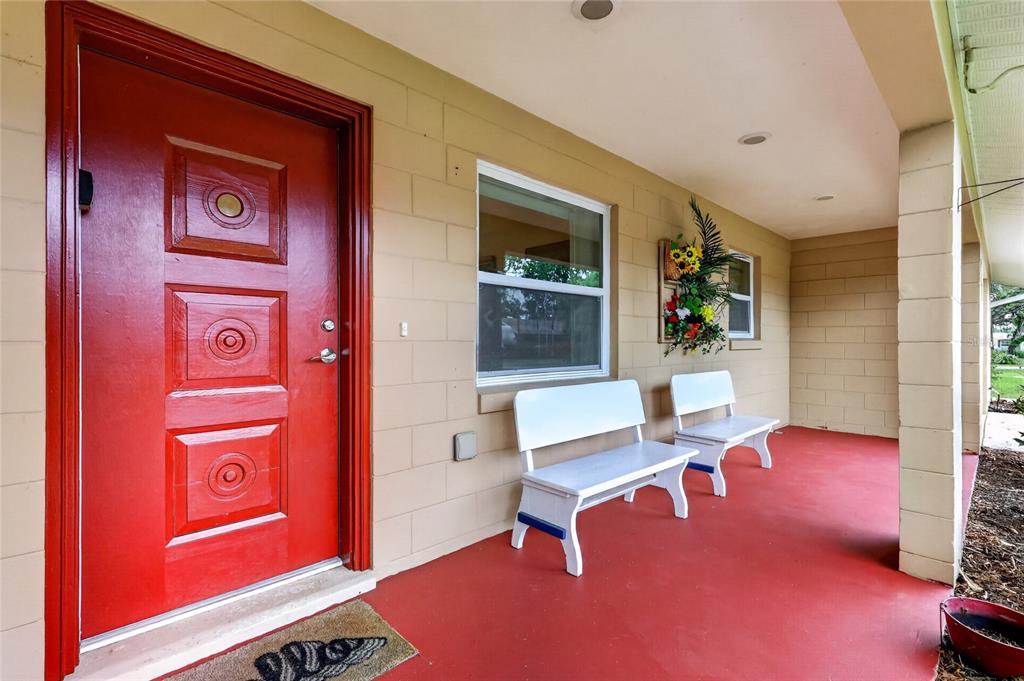 A red front door opens onto a covered porch with white benches and painted flooring — 37414 TURNER DRIVE, UMATILLA, FL