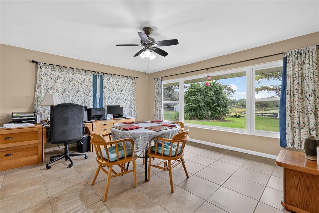 A room with tile flooring, a dining table, a desk, and large windows overlooking greenery — 37414 TURNER DRIVE, UMATILLA, FL