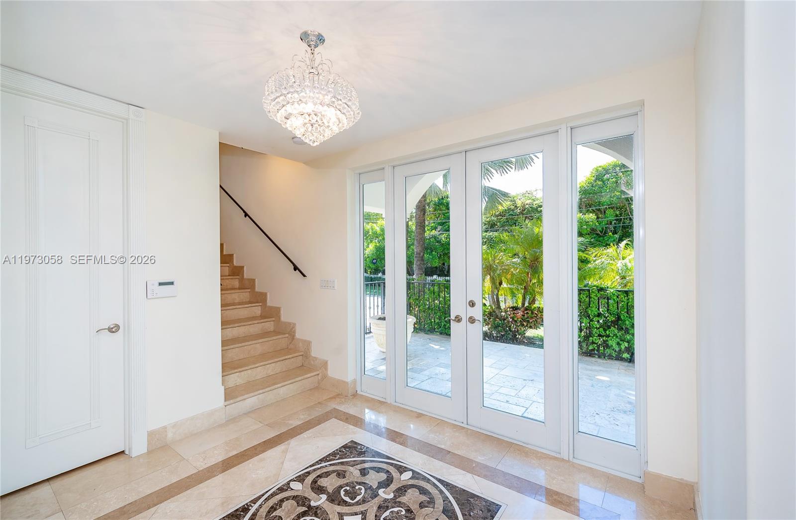 A bright foyer features a crystal chandelier, marble flooring, and glass doors leading outside — 541 S Mashta Dr, Key Biscayne FL 33149, KEY BISCAYNE, FL