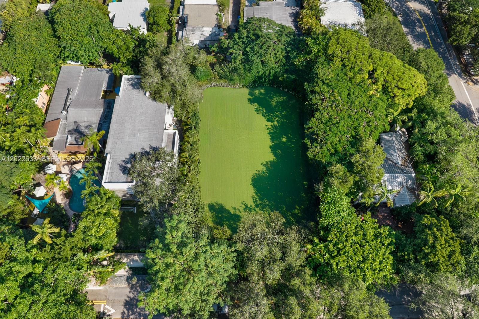 An aerial view shows a rectangular green pond situated between two residential properties and trees — 3729 Kumquat Ave, Miami FL 33133, MIAMI, FL
