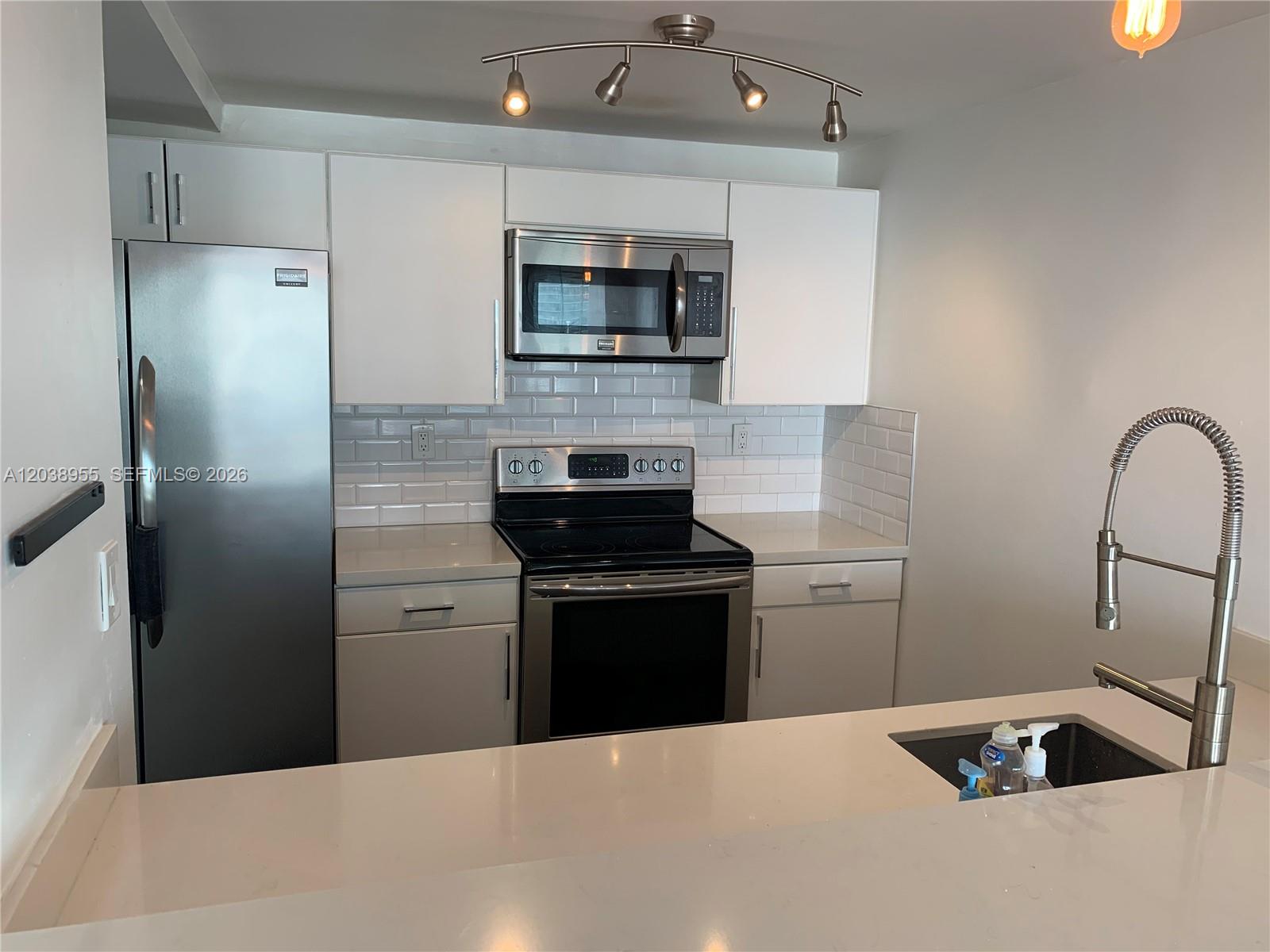 A modern kitchen features white cabinets, stainless steel appliances, a subway tile backsplash, and quartz countertops — 600 NE 36th St # 1017, Miami FL 33137, MIAMI, FL