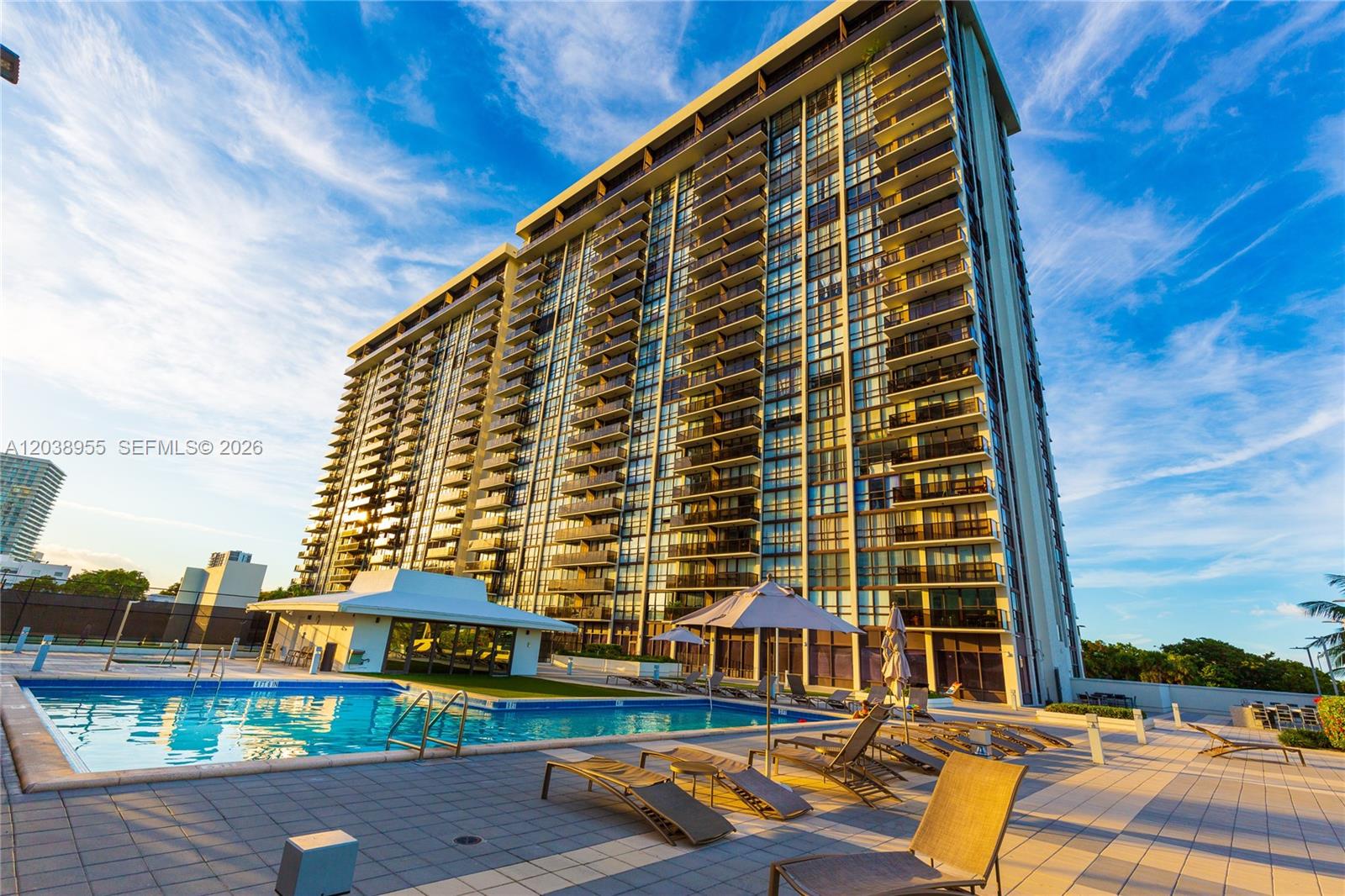 A tall residential building stands beside a swimming pool with lounge chairs and umbrellas — 600 NE 36th St # 1017, Miami FL 33137, MIAMI, FL