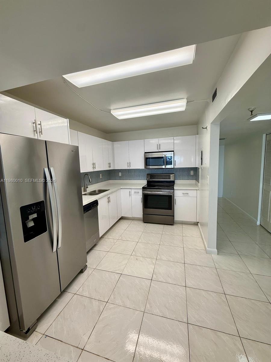 A kitchen features white cabinets, stainless steel appliances, and light-colored tile flooring — 20850 San Simeon Way # 5, Miami FL 33179, MIAMI, FL