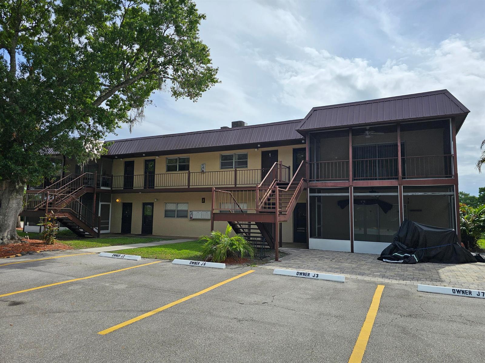A two-story apartment building with exterior staircases, screened balconies, and marked parking spaces — 3124 SE Us Highway 441 # J8, Okeechobee FL 34974, OKEECHOBEE, FL