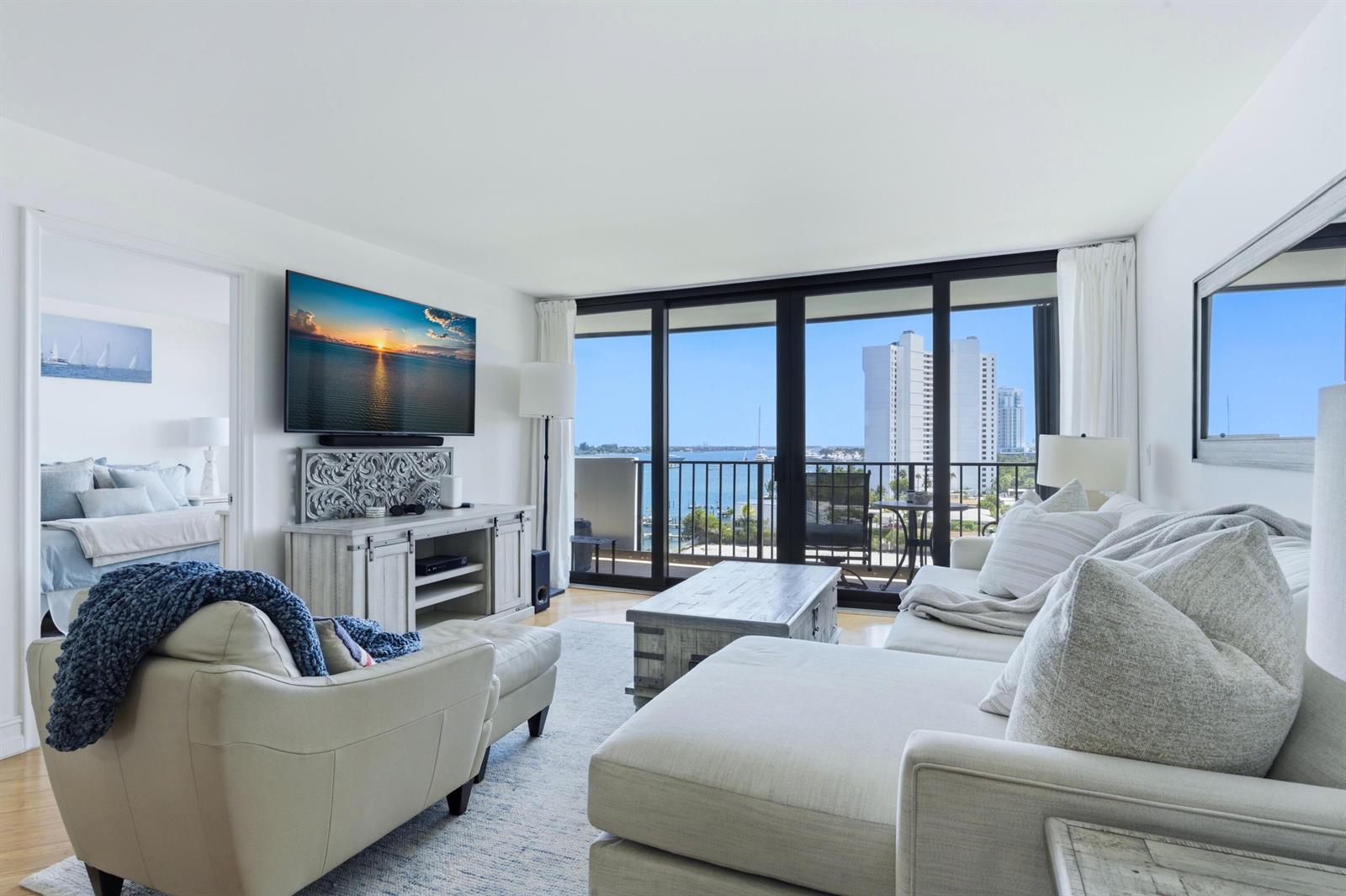 A living room features a sectional sofa, television, and sliding glass doors overlooking the water — 5600 N Flagler Drive Unit 910, West Palm Beach FL 33407, WEST PALM BEACH, FL