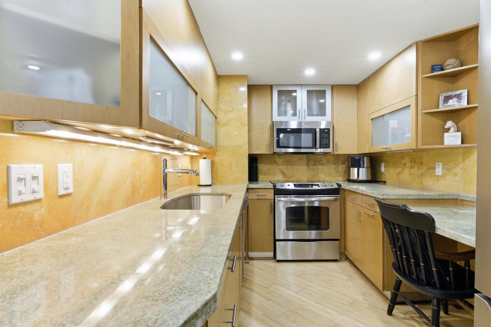 A galley kitchen features light wood cabinets, stone tile backsplash, and stainless steel appliances — 5600 N Flagler Drive Unit 910, West Palm Beach FL 33407, WEST PALM BEACH, FL
