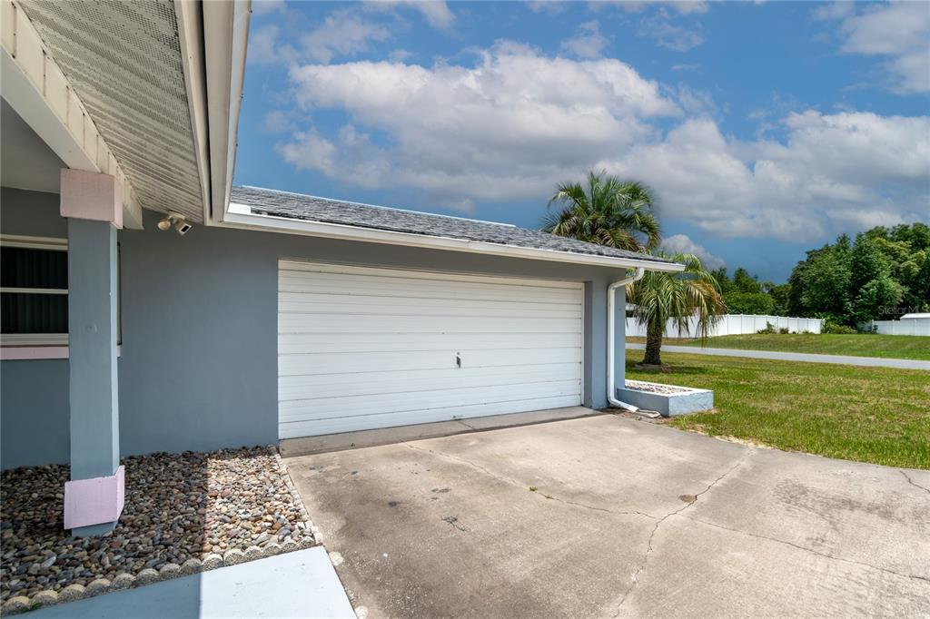 A gray house exterior features a white garage door, a concrete driveway, and a palm tree — 14650 SW 29TH AVENUE ROAD, OCALA, FL