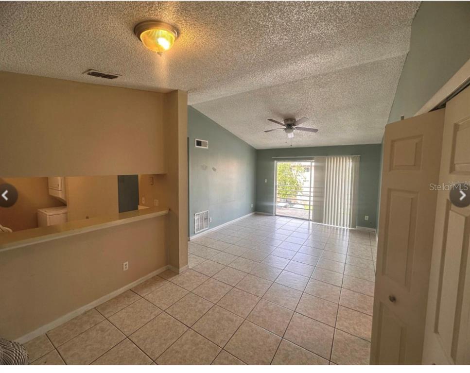 A living room with tile flooring, a vaulted ceiling, and a pass-through to the kitchen — 5213 VIA HACIENDA CIRCLE UNIT 308, ORLANDO, FL