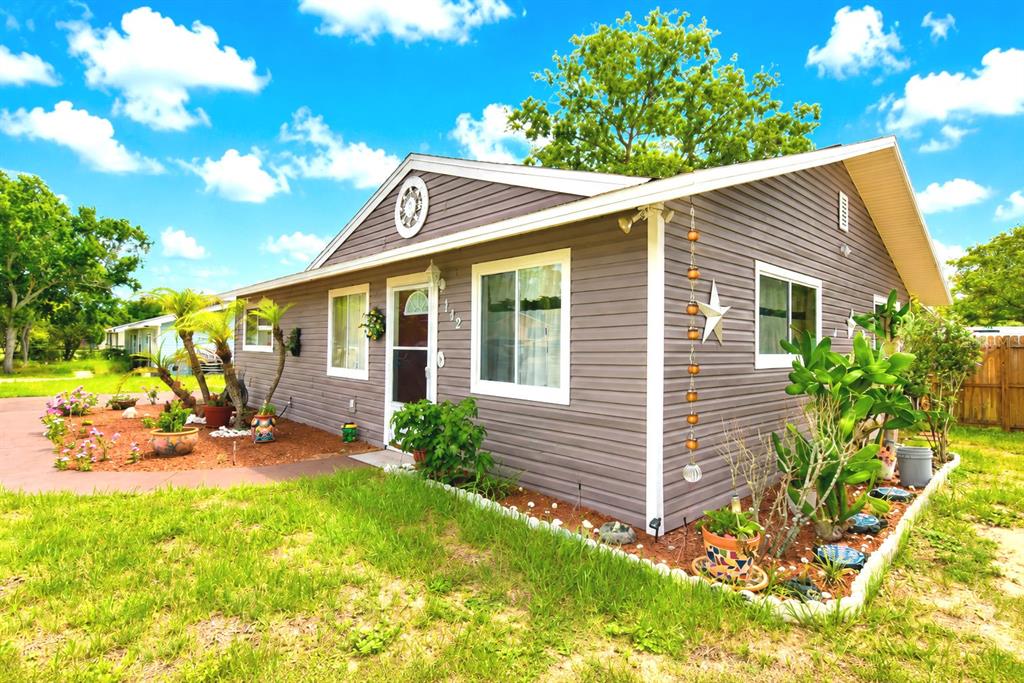 A gray, single-story house with white trim, a front door, and landscaped garden beds — 142 MARTHA DRIVE, LAKE WALES, FL