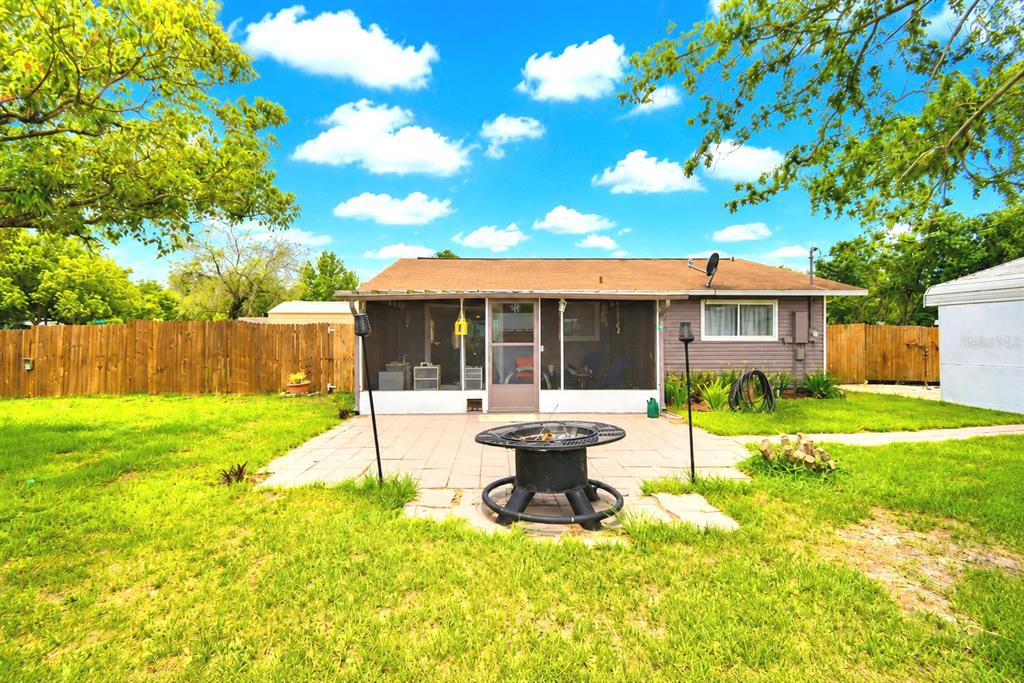 A backyard features a paved patio with a fire pit, a screened porch, and wooden fencing — 142 MARTHA DRIVE, LAKE WALES, FL