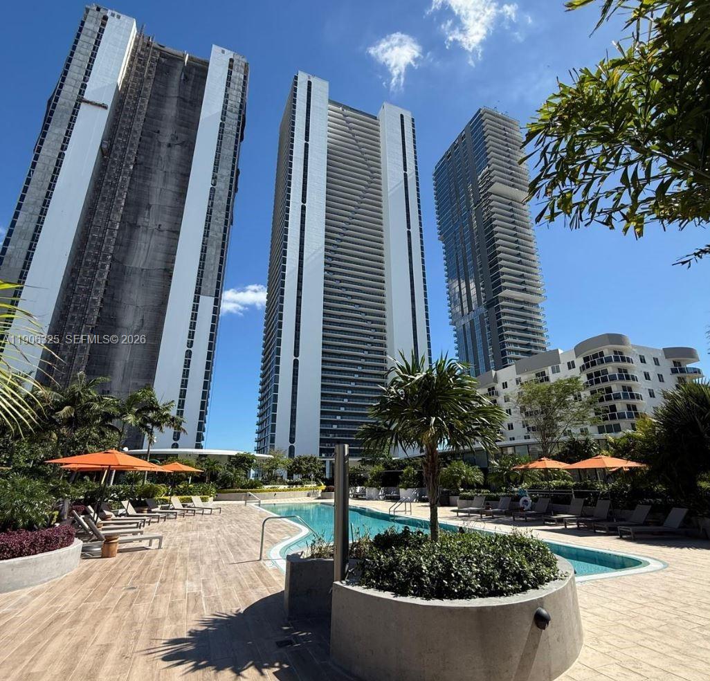 A swimming pool area with lounge chairs and umbrellas sits before three tall skyscrapers — 700 NE 24 # 203, Miami FL 33137, MIAMI, FL