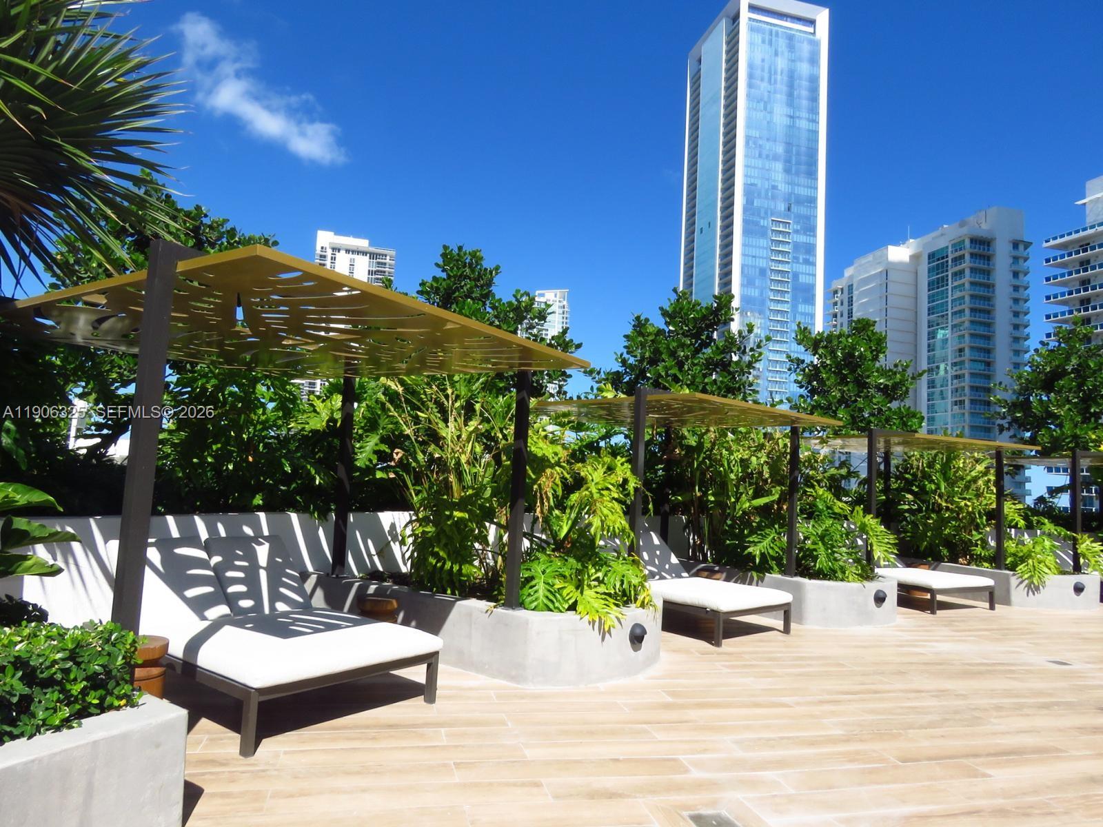 A rooftop terrace features lounge chairs under decorative metal pergolas surrounded by lush green plants — 700 NE 24 # 203, Miami FL 33137, MIAMI, FL