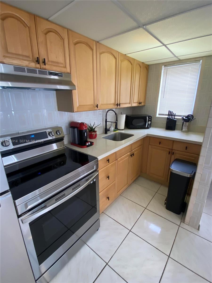 A kitchen features light wood cabinets, stainless steel appliances, white countertops, and white tile flooring — 3210 Canal Dr # 8, Pompano Beach FL 33062, POMPANO BEACH, FL