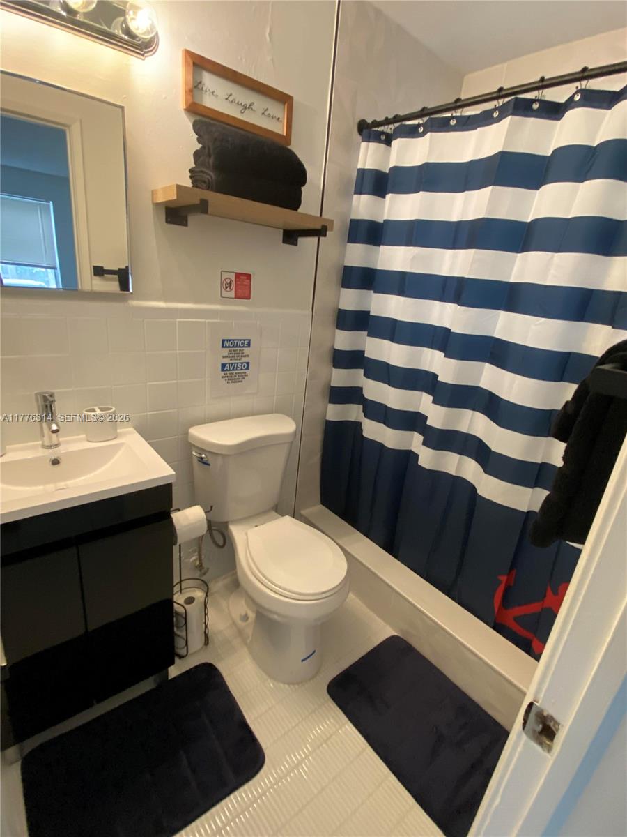 A bathroom features a white vanity, a toilet, and a blue and white striped shower curtain — 3210 Canal Dr # 8, Pompano Beach FL 33062, POMPANO BEACH, FL