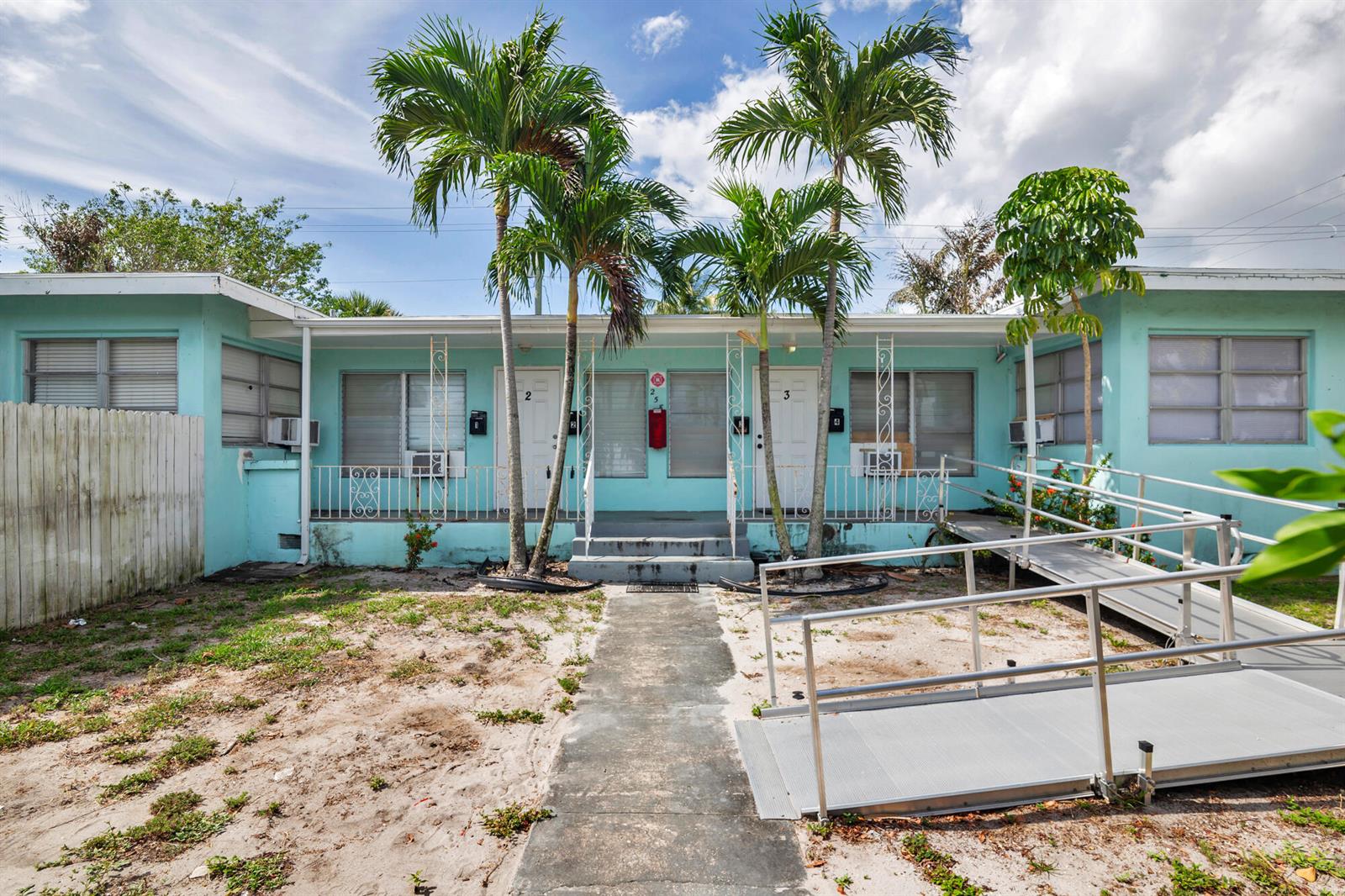 A single-story, light blue apartment building features a central walkway, palm trees, and a metal ramp — 258 Conniston Road, West Palm Beach FL 33405, WEST PALM BEACH, FL