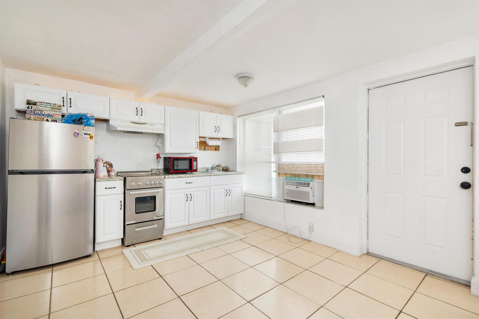 A kitchen features white cabinets, stainless steel appliances, tile flooring, and a window air conditioner — 258 Conniston Road, West Palm Beach FL 33405, WEST PALM BEACH, FL