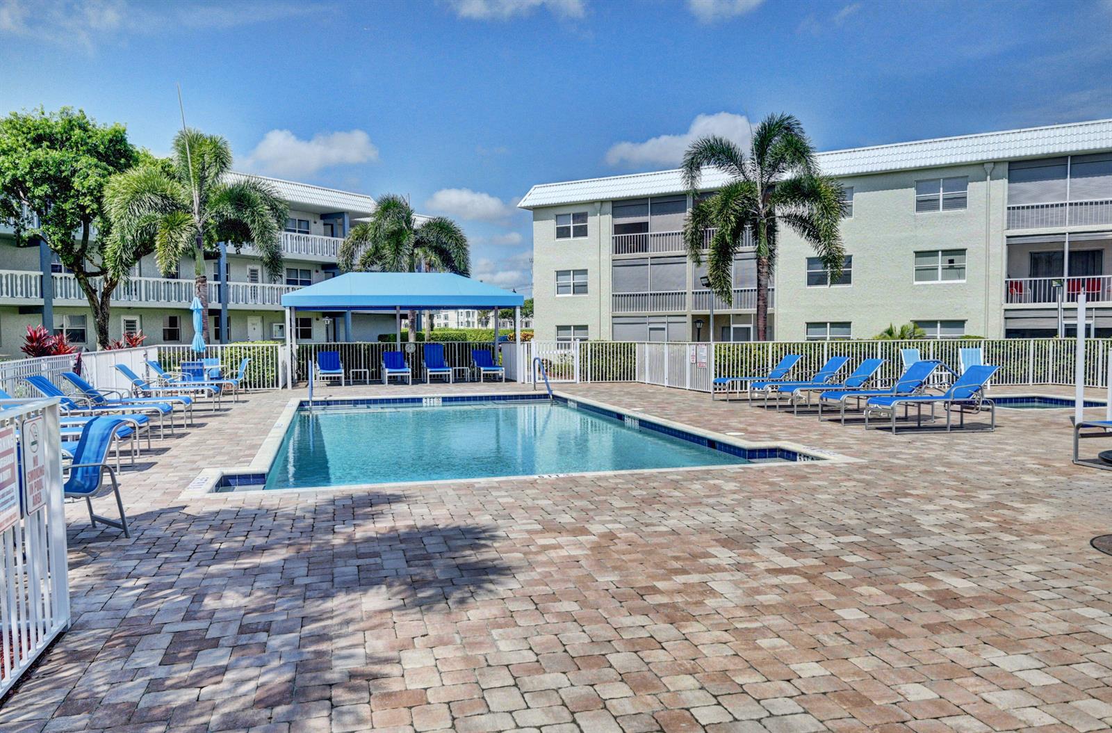 A swimming pool with lounge chairs and a blue canopy sits between two apartment buildings — 9826 Marina Boulevard # 1027, Boca Raton FL 33428, BOCA RATON, FL