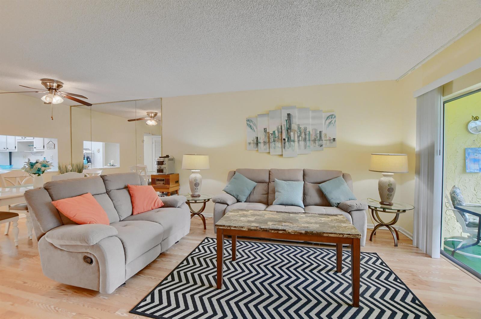 A living room features two gray sofas, a chevron rug, and a large wall mirror — 9826 Marina Boulevard # 1027, Boca Raton FL 33428, BOCA RATON, FL