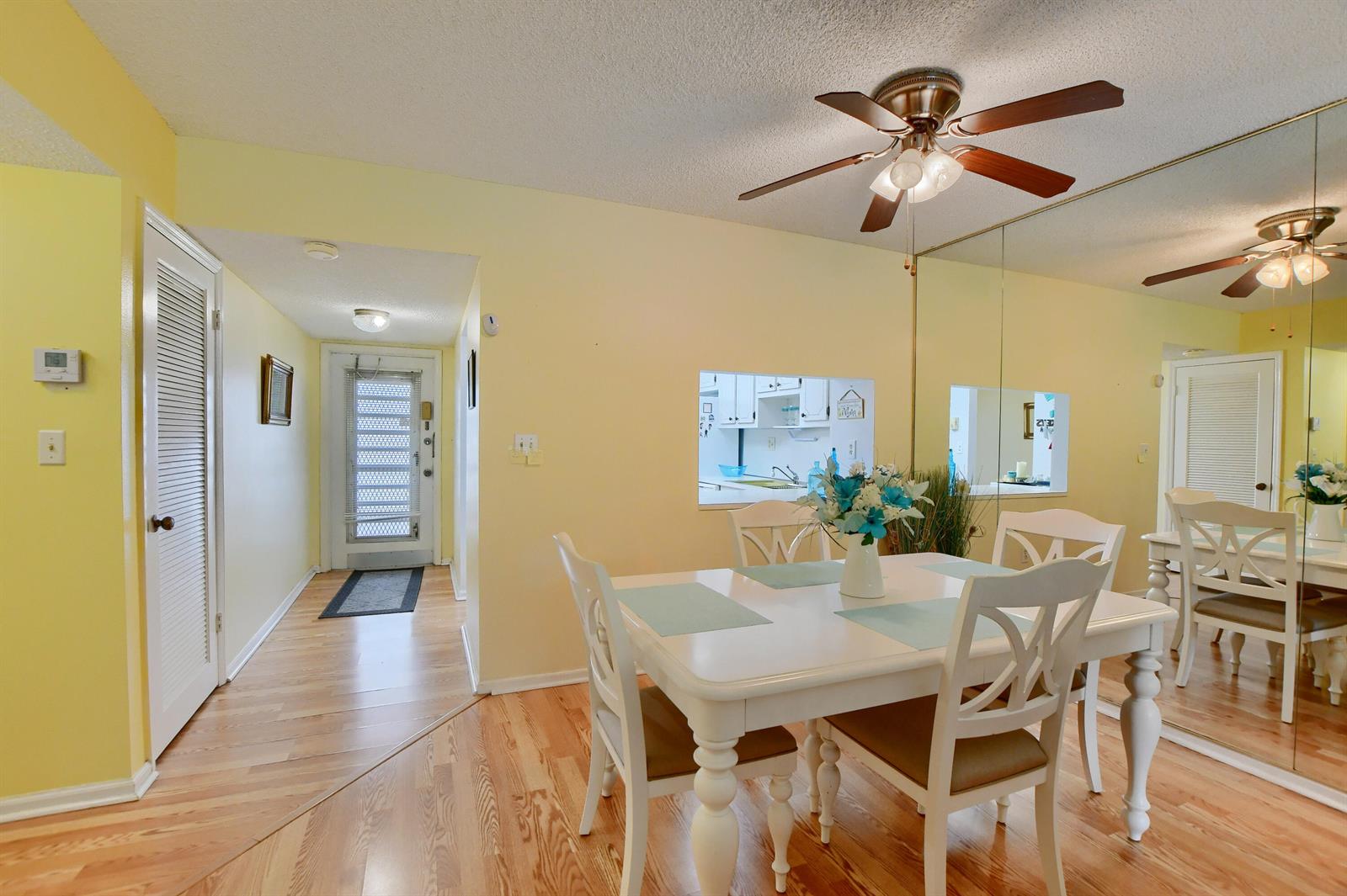 A dining area with a white table, chairs, and a mirrored wall facing a kitchen pass-through — 9826 Marina Boulevard # 1027, Boca Raton FL 33428, BOCA RATON, FL