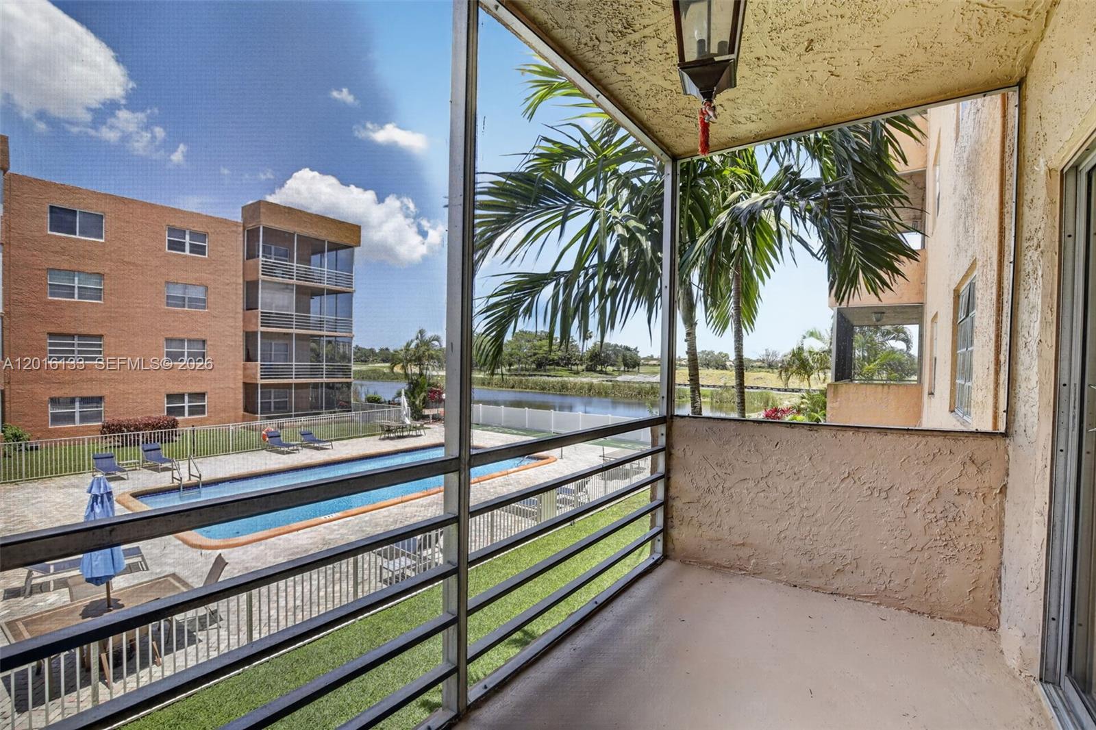 A screened balcony overlooks a swimming pool, a pond, and a multi-story apartment building — 3048 E Sunrise Lakes Dr # 220, Sunrise FL 33322, SUNRISE, FL