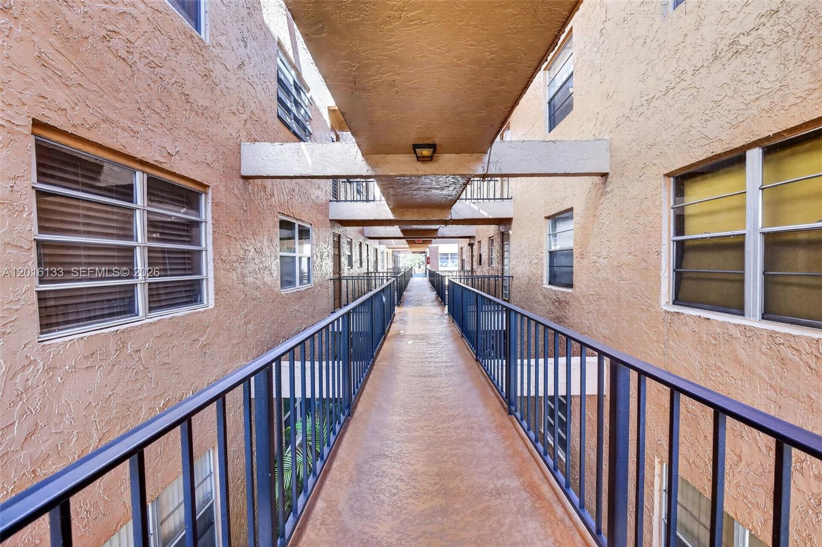 An outdoor walkway connects two apartment buildings with stucco walls and metal railings — 3048 E Sunrise Lakes Dr # 220, Sunrise FL 33322, SUNRISE, FL