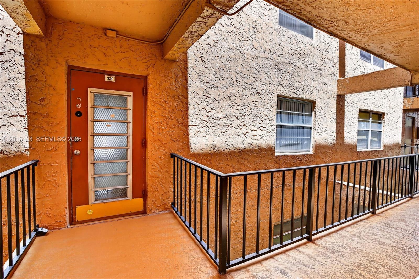 An exterior view of an apartment entrance with an orange door and metal railing — 3048 E Sunrise Lakes Dr # 220, Sunrise FL 33322, SUNRISE, FL