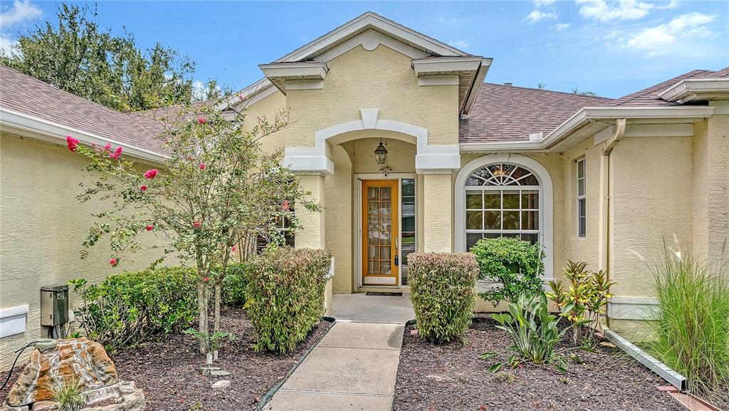 The exterior of a beige stucco house features a covered entryway with a wooden door — 6521 SUNDEW COURT, BRADENTON, FL