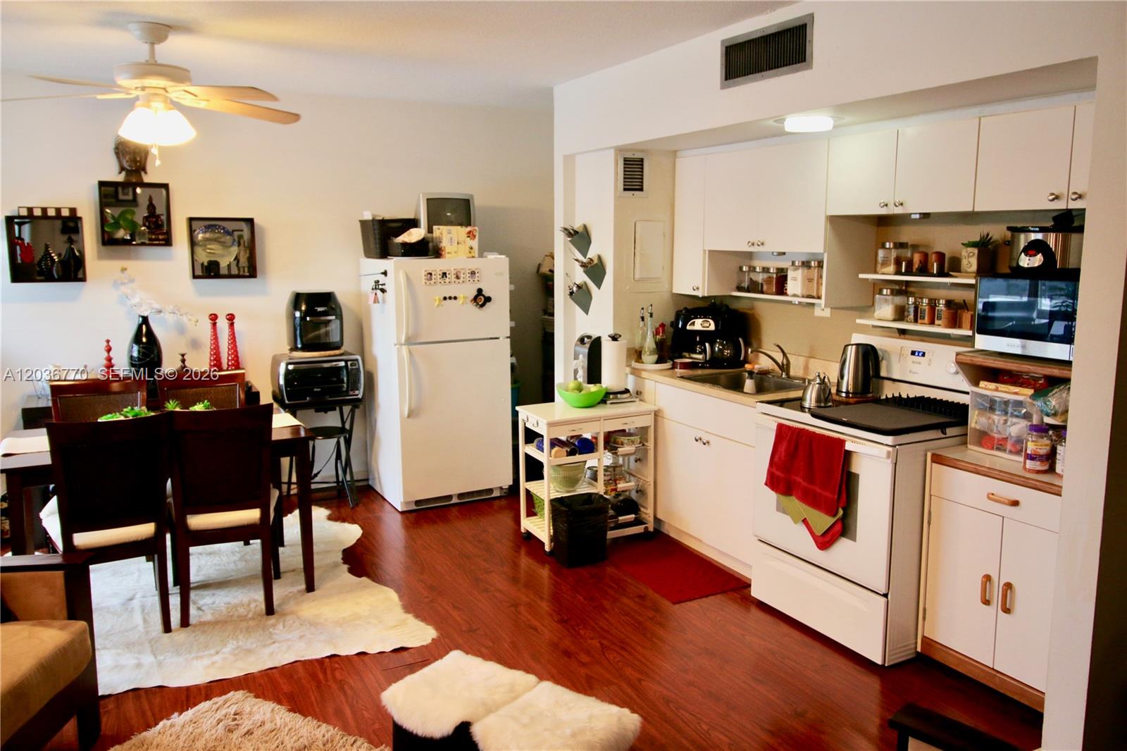 A kitchen and dining area features white cabinetry, white appliances, and dark wood-look flooring — 900 Bay Dr # 215, Miami Beach FL 33141, MIAMI BEACH, FL