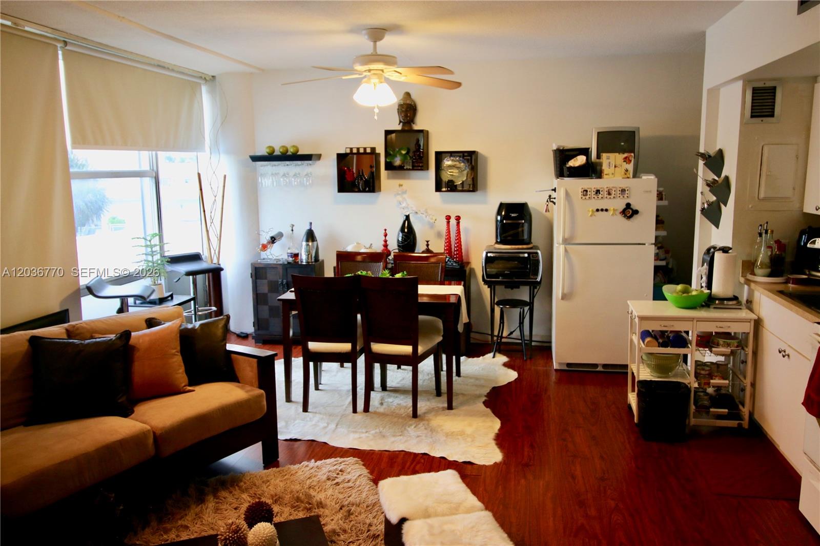 An open-concept living and dining area features wood flooring, a ceiling fan, and white walls — 900 Bay Dr # 215, Miami Beach FL 33141, MIAMI BEACH, FL