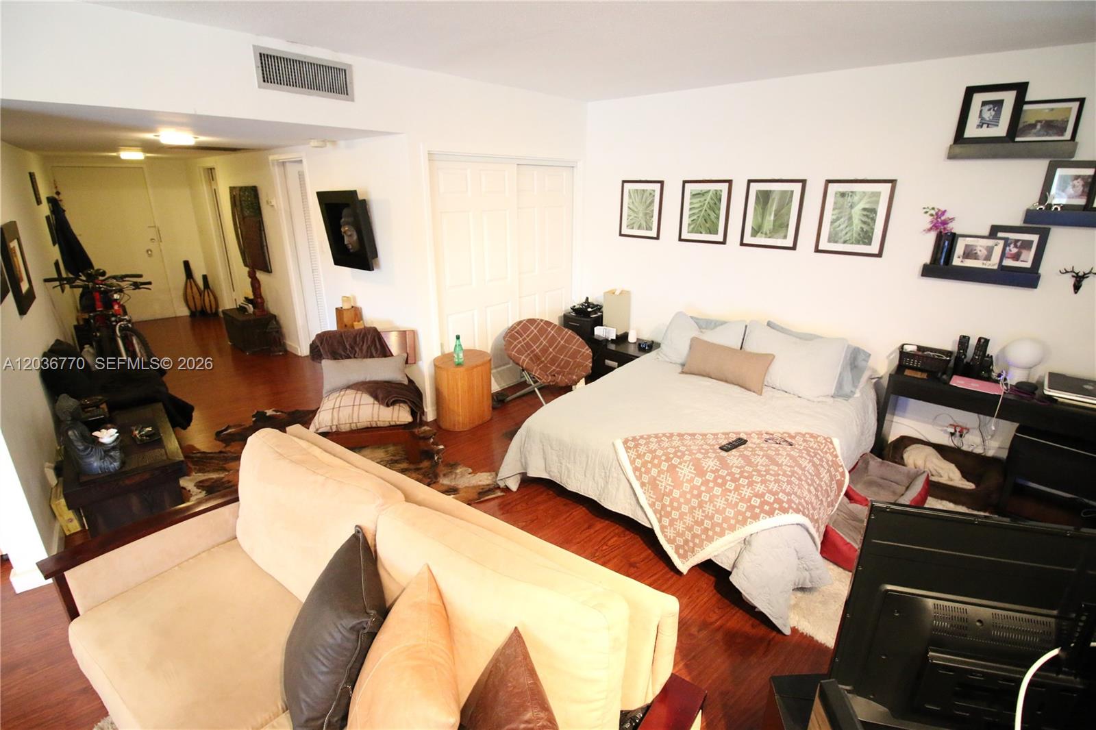 A studio apartment features a bed, sofa, wood flooring, and wall-mounted decor — 900 Bay Dr # 215, Miami Beach FL 33141, MIAMI BEACH, FL