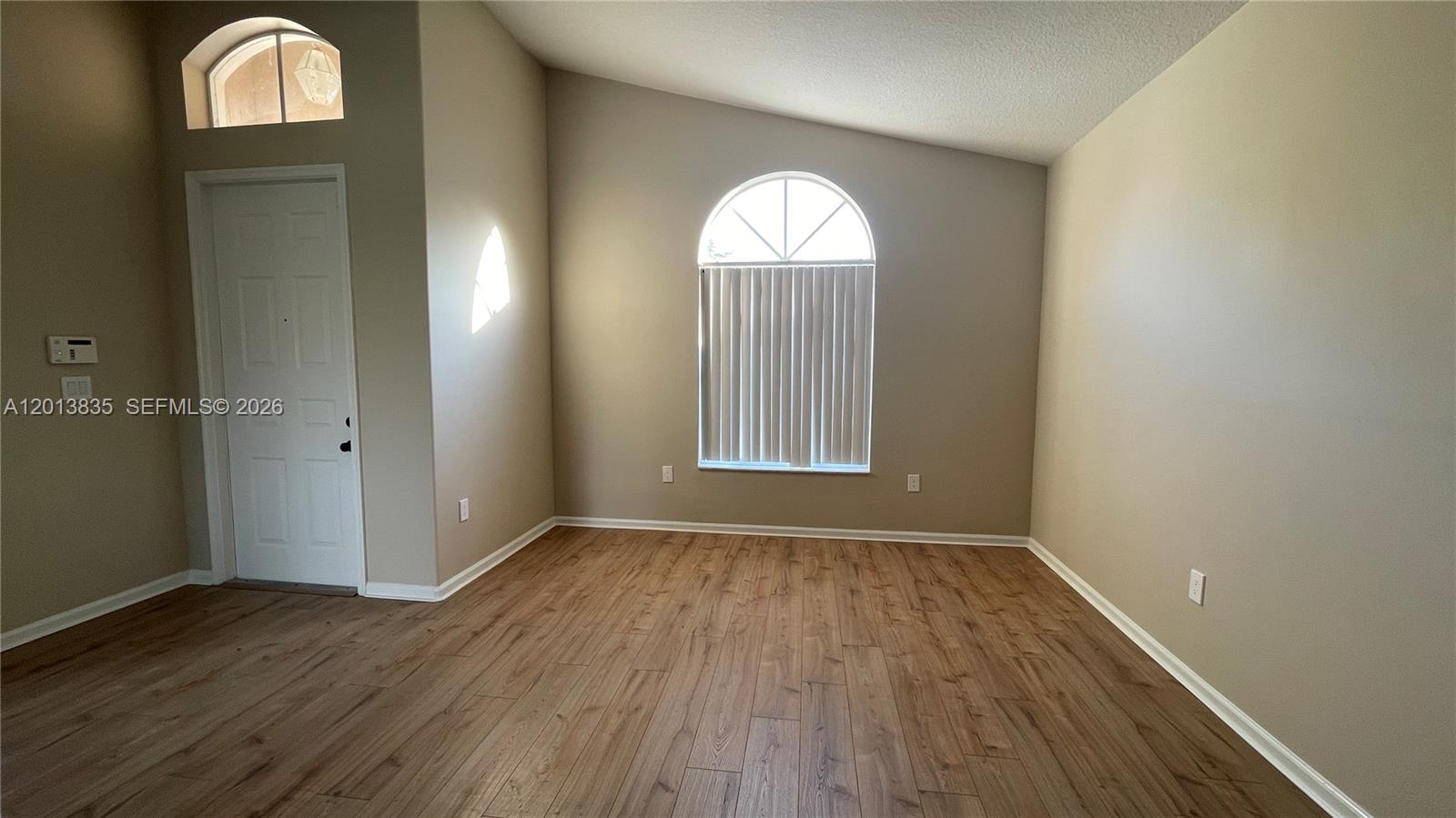 An empty room features light-colored walls, wood-look flooring, and a large arched window with blinds — 18811 SW 29th Ct, Miramar FL 33029, MIRAMAR, FL